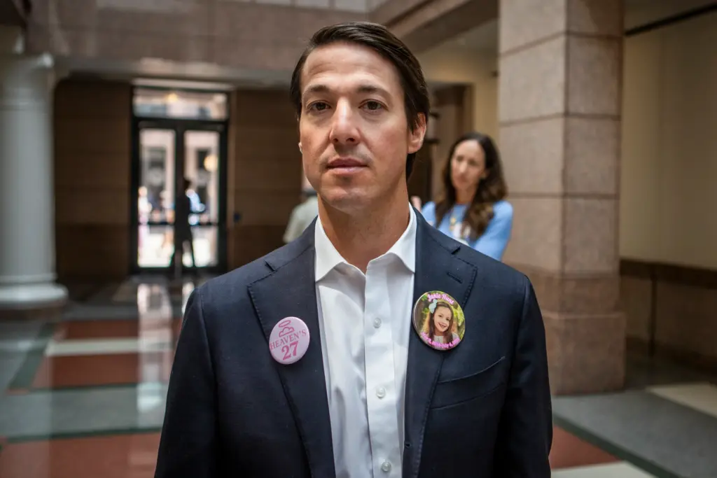 Davin Hunt, father of 9-year-old Janie Hunt who passed away during the Camp Mystic flood, poses for a portrait during a pause in the committee hearing intermission on Thursday. Hunt was one of several family members who wore pins in honor of their loved ones.