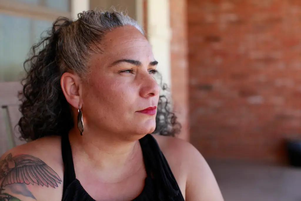 Air Force veteran Omaira Garcia sits on her front porch in Abilene, Texas. She says dust kicked up by construction of OpenAI’s flagship data center next door regularly covers her property. “Coming outside to enjoy time out here has become really difficult for us.” she says.