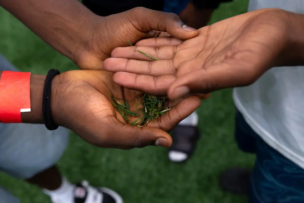 Theogene Bikeombe, left, hands Kenasi Mwami blades of grass from the pitch used by the World Cup players during a tour of the NRG Stadium in Houston on July 5, 2026.