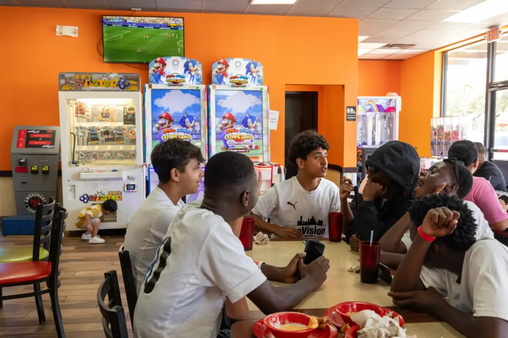 The Houston reVision team eat at Cicis Pizza after taking a tour of the World Cup stadium together as the Brazil vs Norway match plays in the background, Sunday, July 5, 2026, in Houston. (Antranik Tavitian for The Texas Tribune)