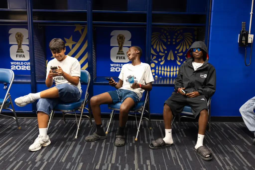 Arian Yousofi, Kenasi Mwami and Moises Badera, left to right, laugh as they sit in the locker room used by the Moroccan national team days earlier in their World Cup match, in early July.