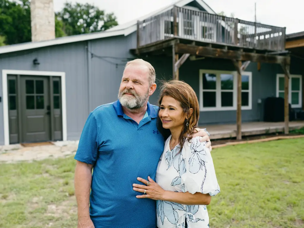 Mike Trolinger, a retired San Antonio Police officer from Kerrville, and his wife Brenda Espinoza outside of their home in Ingram on June 12, 2026. The couple renovated their home after the Kerr County flood caused significant damage.