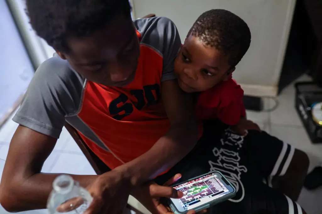Moises Badera watches highlights of the Portugal vs Uzbekistan World Cup match to see if he can spot himself while Rene Ngongo tries to get his attention.