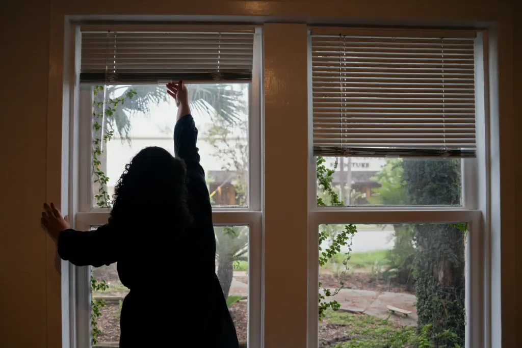 Silvina opens her window blinds at her home on July 14, 2026, in Houston, Texas.