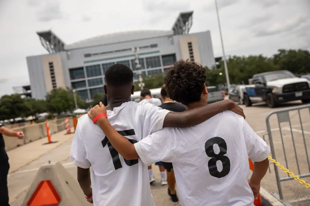 Joel Lwamba, at left, and Zaki Yousofi, hold onto each other as they walk towards the Houston World Cup stadium for a tour, Sunday, July 5, 2026, in Houston.