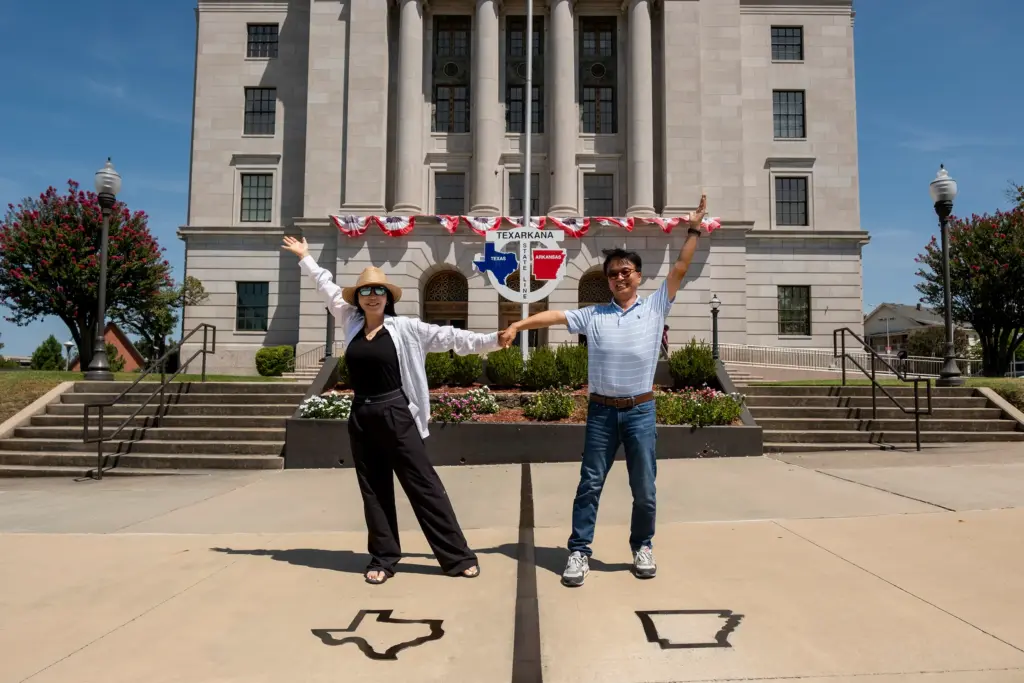 Mikyoung Hong and Cheoungjoon Lee of Korea hold hands while standing in different states at the State Line Post Office and Federal Building on the Texas/Arkansas border in downtown Texarkana on Wednesday. The massive Smackover Formation extends from Texas across Arkansas, Louisiana, Mississipi, alabama and Florida.